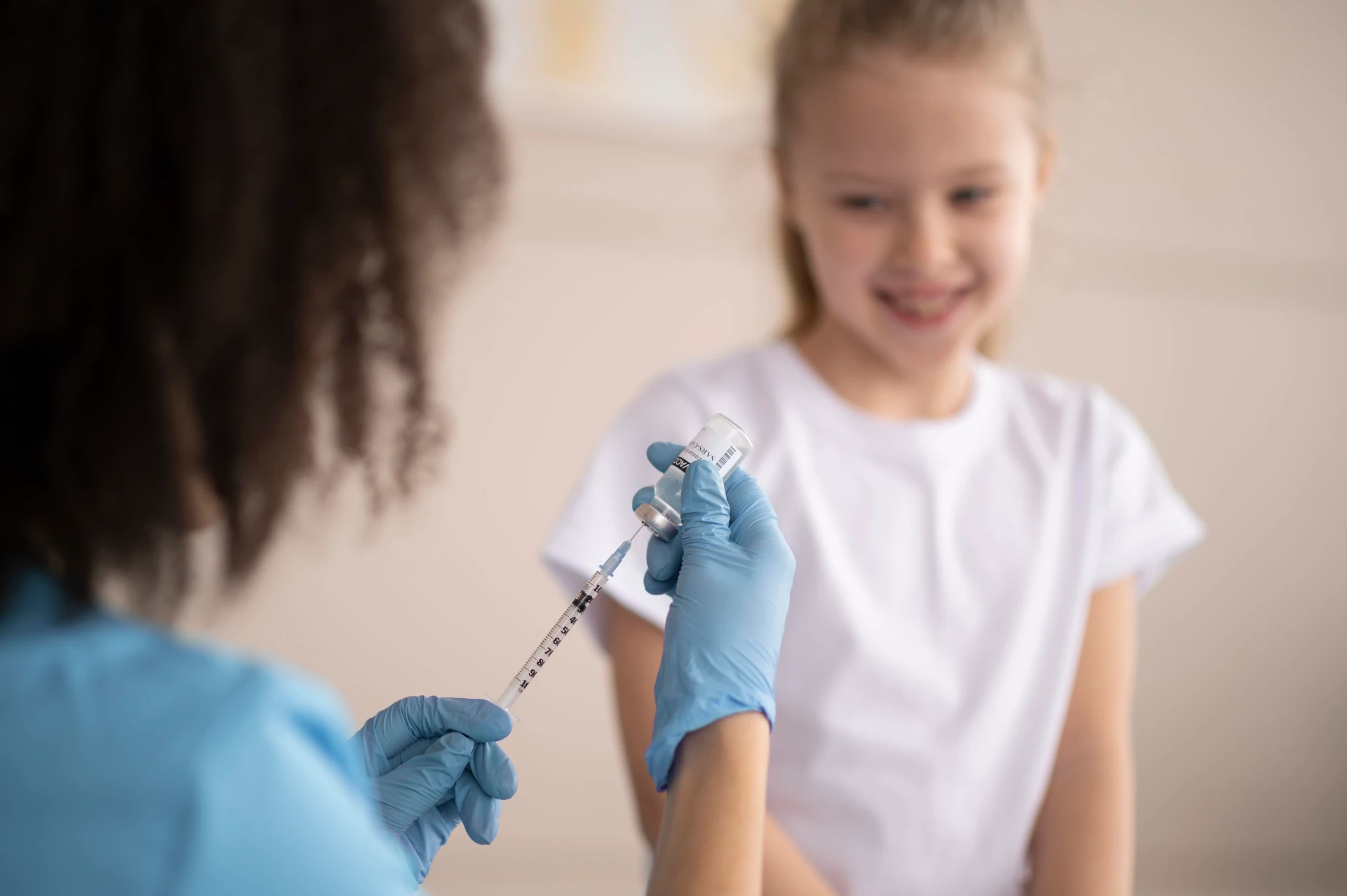 enfermeira enchendo seringa para aplicar injeção em menina loira pré-adolocente.